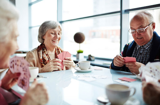 Four seniors sit around a table playing cards. coffee cups are in front of each person.