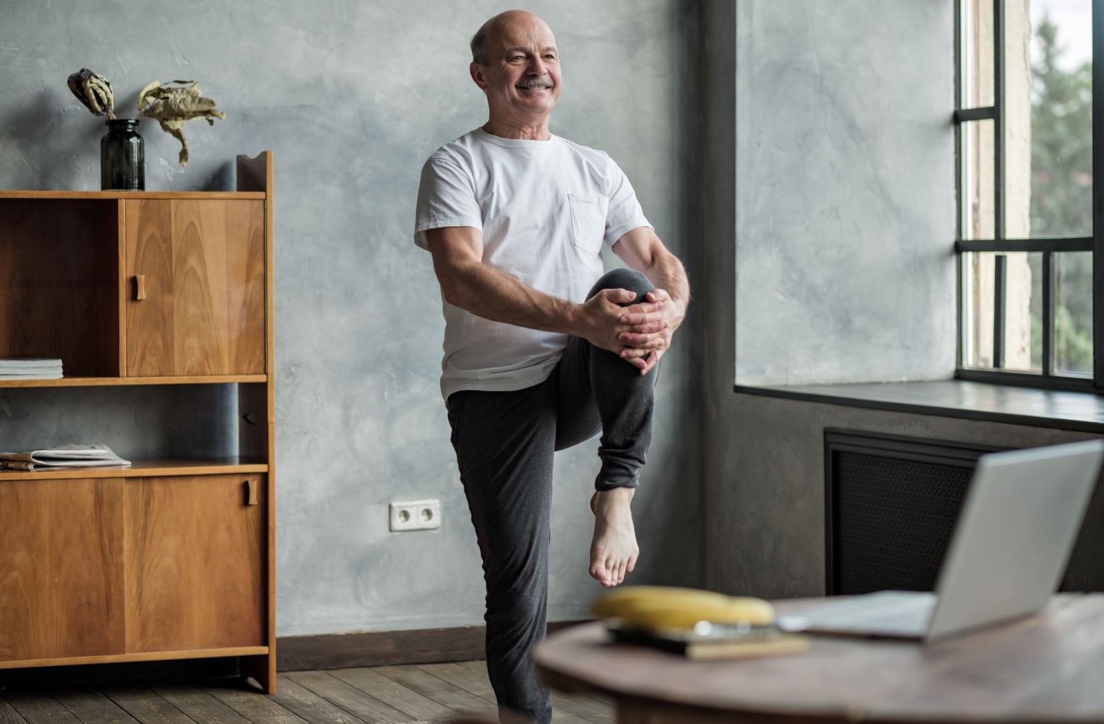 A senior man standing on one leg, with his other leg lifted slightly off the ground.