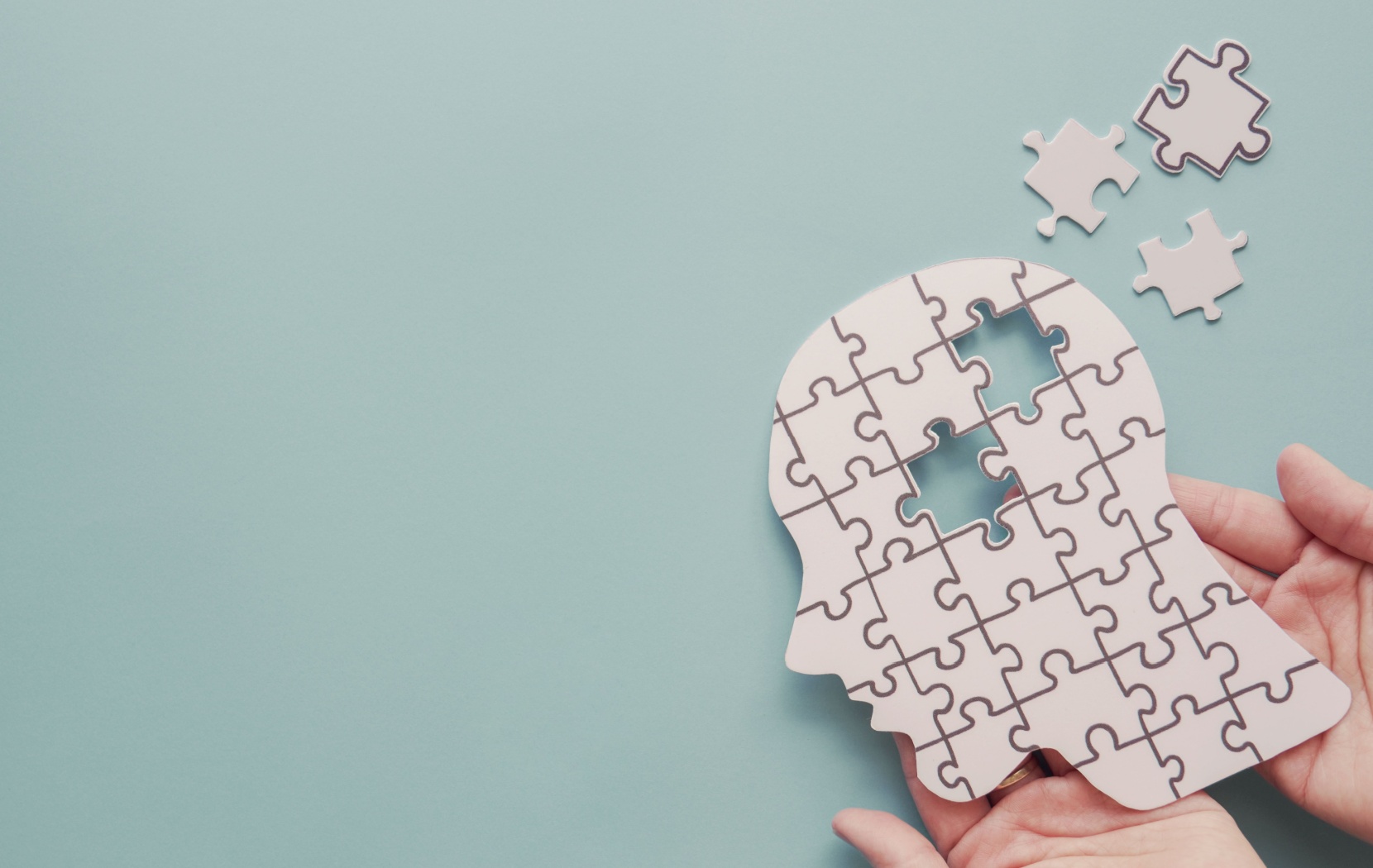 Two hands hold up a puzzle of a person's head. Two pieces missing to symbolize the cognitive decline of dementia.