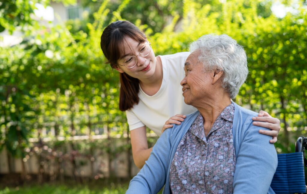A caretaker smiles at an older adult with dementia while on a together walk outside.